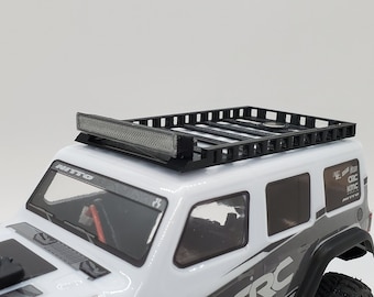 Pode incluir: Um jipe de brinquedo branco com um rack de teto preto e uma barra de luz no topo. O jipe tem um interior preto e rodas pretas.