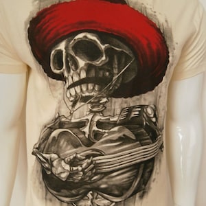 May include: A white t-shirt with a black and white illustration of a skeleton wearing a red sombrero and playing a guitar.