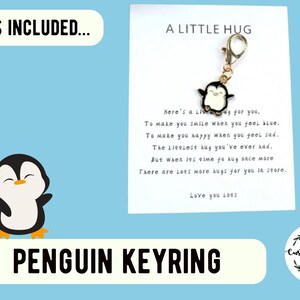 Puede incluir: Una tarjeta blanca con texto negro que dice "A Little Hug" y un poema sobre abrazos. Un peque&ntilde;o llavero de ping&uuml;ino blanco y negro est&aacute; unido a la tarjeta. La tarjeta est&aacute; sobre un fondo azul claro con el texto "What's Included..." y "Penguin Keyring" en negro.