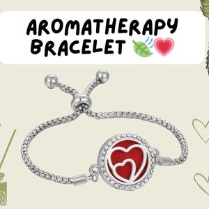 May include: Silver aromatherapy bracelet with a round pendant featuring two red hearts. The bracelet has an adjustable sliding clasp.