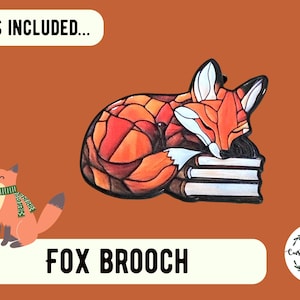 May include: A fox brooch featuring a stained-glass style design of a fox sleeping on a stack of books, with orange, red, and white colors. A small cartoon fox wearing a green scarf is also present. Text includes WHAT'S INCLUDED and FOX BROOCH.