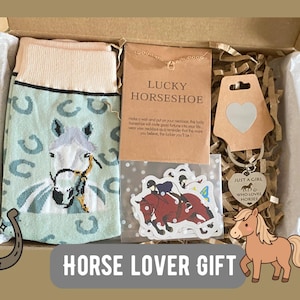 Könnte beinhalten: Eine Geschenkbox mit hellgrünen Socken mit Pferde- und Hufeisenmuster, einer Lucky Horseshoe Halskette auf einer Karte, einem Set mit Pferdeaufklebern und einem silbernen herzförmigen Schlüsselanhänger mit dem Text Just a Girl Who Loves Horses.