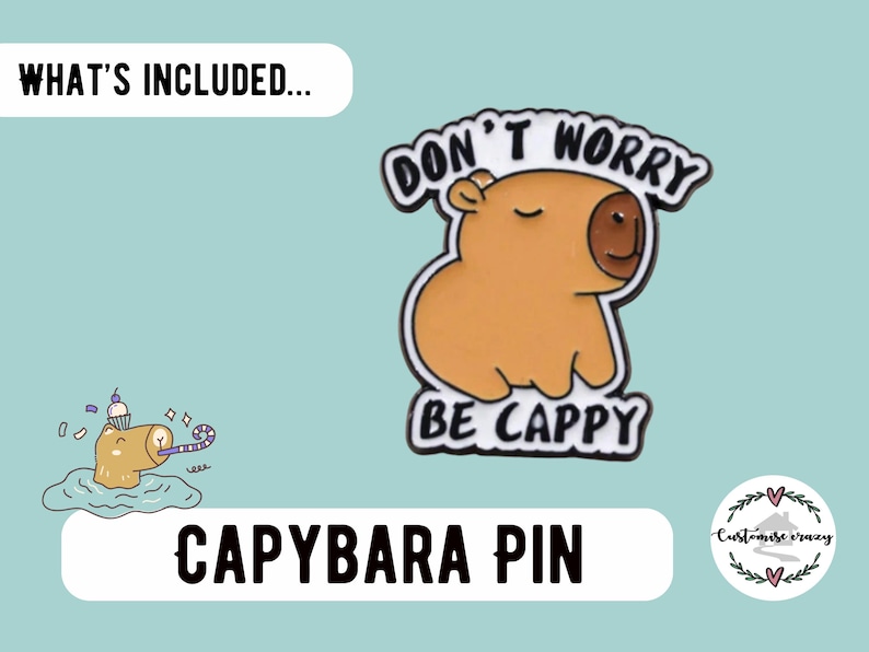May include: A capybara pin with the text "DON'T WORRY BE CAPPY". The pin features a cartoon capybara in shades of brown and tan with a black outline. The image also includes a small illustration of a capybara with a party hat.