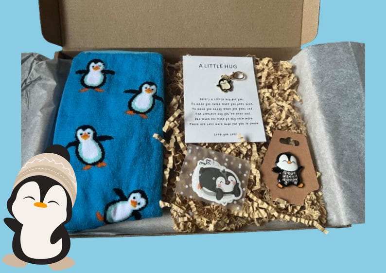 Puede incluir: Un calcet&iacute;n azul y blanco con estampado de ping&uuml;ino, una pegatina de ping&uuml;ino blanco y negro, un amuleto de ping&uuml;ino blanco y negro, una tarjeta marr&oacute;n con un amuleto de ping&uuml;ino blanco y negro y una tarjeta con el texto "A Little Hug" y un mensaje sobre enviar un abrazo.