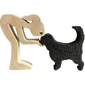 May include: A gold-coloured sculpture of a person leaning down to kiss a black dog sculpture.