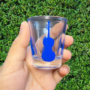 May include: A clear glass shot glass with a blue silhouette of a violin on the front.