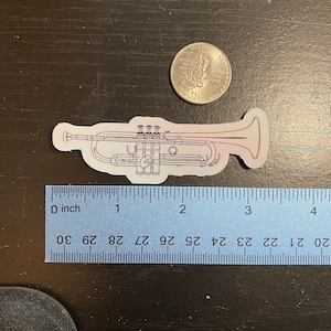 May include: A white and purple outline sticker of a trumpet with a silver US quarter for scale. The sticker is approximately 3 inches long.