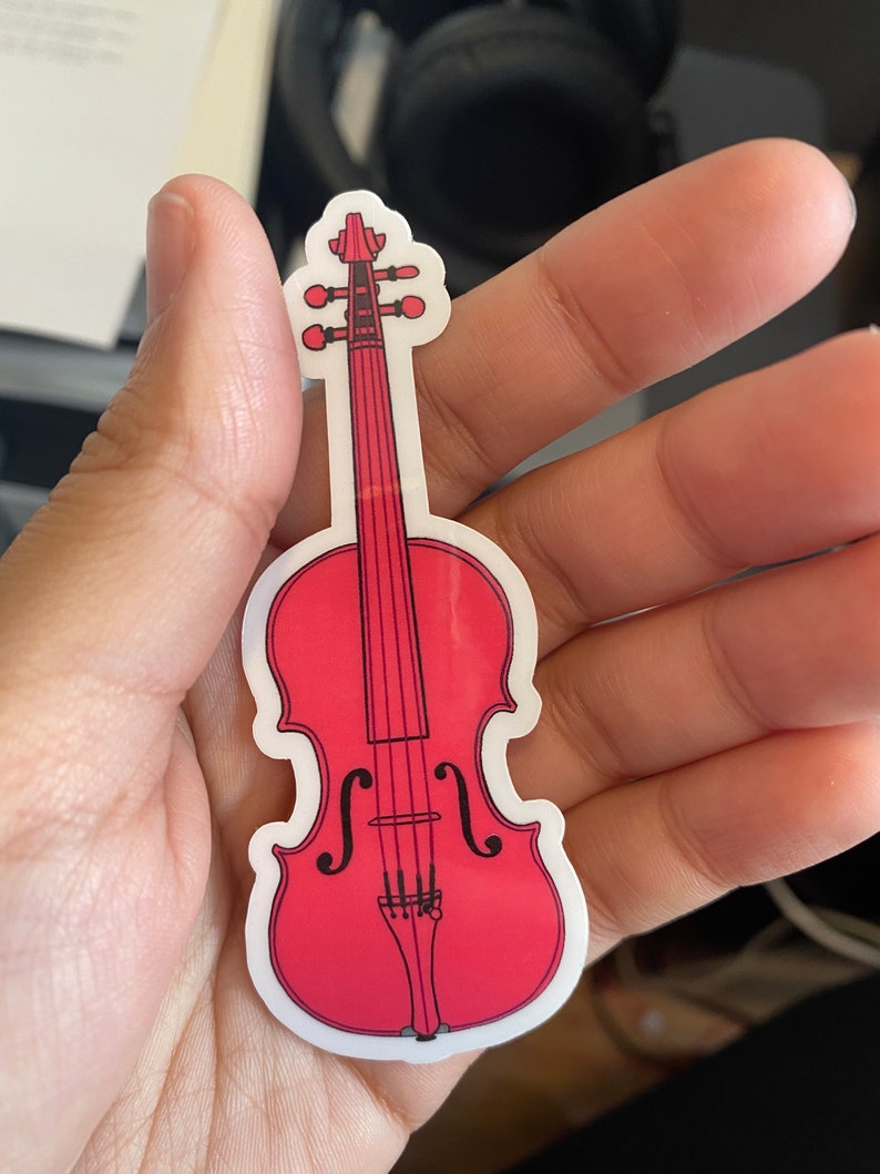 Puede incluir: Una pegatina de viol&iacute;n roja con contornos y detalles negros. La pegatina est&aacute; sobre un fondo blanco.