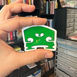 May include: A green vinyl sticker of a violin's f-hole, a common symbol for music and musicians.