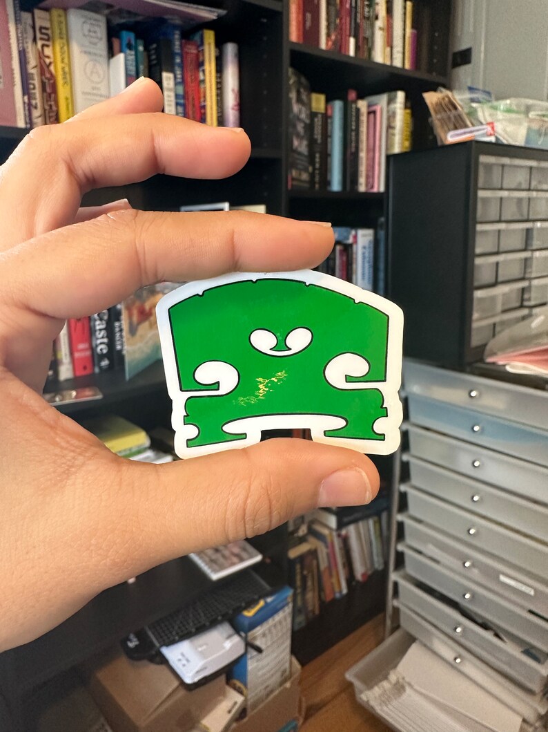 May include: A green vinyl sticker of a violin's f-hole, a common symbol for music and musicians.
