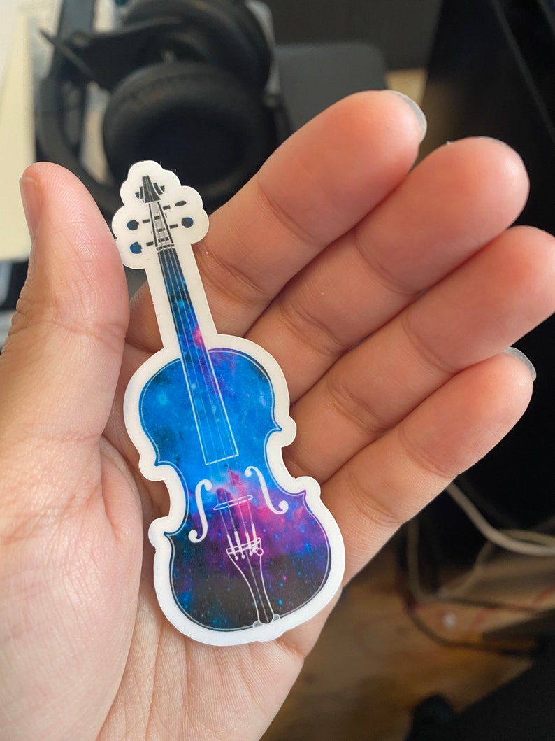 Puede incluir: Una pegatina de vinilo de un viol&iacute;n con un dise&ntilde;o de galaxia. El viol&iacute;n est&aacute; contorneado en blanco y el dise&ntilde;o de la galaxia est&aacute; en tonos de azul, morado y rosa.