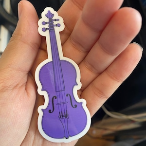 Puede incluir: Una pegatina de vinilo morado de un viol&iacute;n con un contorno blanco.