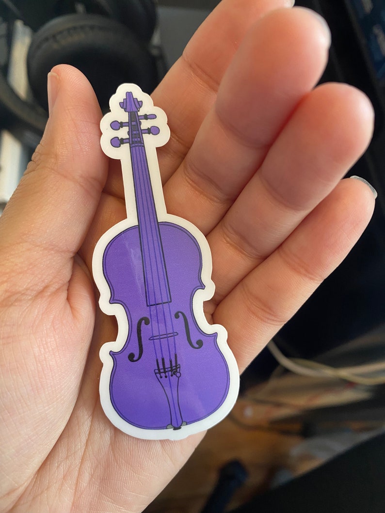 Puede incluir: Una pegatina de vinilo morado de un viol&iacute;n con un contorno blanco.