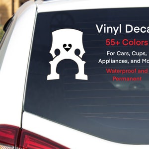 May include: White vinyl decal of a bass clef with a heart on the top. The decal is on the back window of a car. The text "Vinyl Decal 55+ Colors For Cars, Cups, Appliances, and More Waterproof and Permanent" is below the decal.