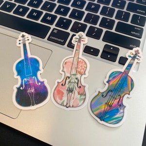 Puede incluir: Tres pegatinas de vinilo de violines con diferentes dise&ntilde;os. Un viol&iacute;n tiene un dise&ntilde;o de galaxia, otro tiene un dise&ntilde;o floral y el tercero tiene un dise&ntilde;o hologr&aacute;fico.
