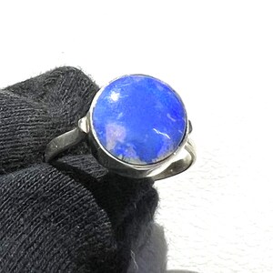 Op de afbeelding: Een zilveren ring met een blauwe opaal edelsteen. De opaal is rond en is gezet in een bezel setting.