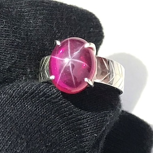 May include: A silver ring featuring a pink star ruby gemstone. The ring has a textured band.