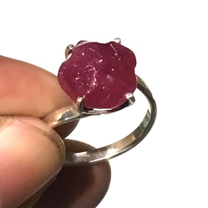 Puede incluir: Un anillo de plata con una gran piedra preciosa de rubí tallada en bruto. El rubí es de color rojo intenso y tiene un aspecto natural sin pulir.