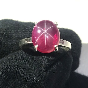 May include: A silver ring with a large, oval-shaped, red star ruby gemstone.