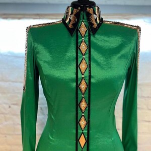 May include: A green long-sleeved shirt with a black and gold geometric design. The shirt has a pointed collar and a button-up front.