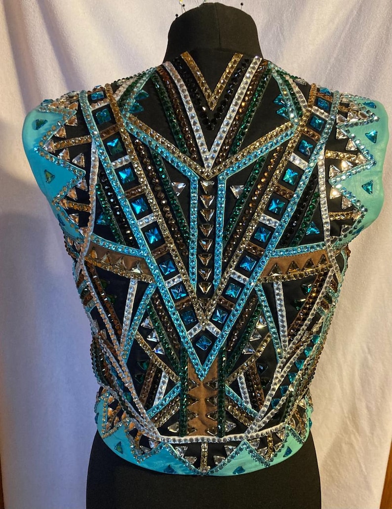 May include: A turquoise, black, green, gold and white show vest with a geometric design. The vest is made of mesh fabric and is embellished with rhinestones.