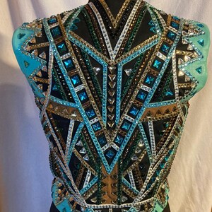 May include: A turquoise, black, green, gold and white show vest with a geometric design. The vest is made of mesh fabric and is embellished with rhinestones.