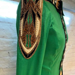 May include: A green long-sleeved shirt with a black, gold, and white patterned design on the shoulder. The shirt has a satin finish.