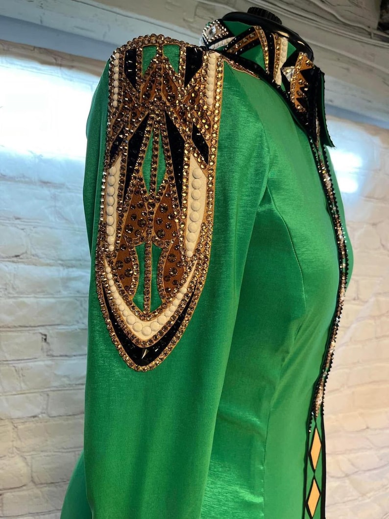 May include: A green long-sleeved shirt with a black, gold, and white patterned design on the shoulder. The shirt has a satin finish.