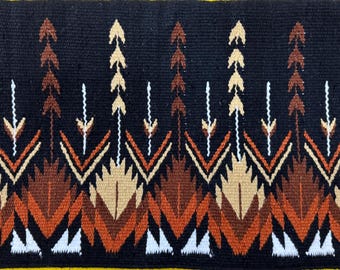 May include: A black saddle blanket with a geometric pattern in shades of brown, orange, and white. The pattern features stylized arrows and leaves.