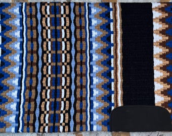 May include: A black and blue saddle pad with a geometric pattern. The pad has a brown leather cinch strap.