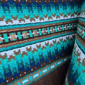Pode incluir: Um close-up de um tecido tecido marrom e azul com um padr&atilde;o geom&eacute;trico. O tecido tem uma faixa branca que atravessa o centro e &eacute; feito de um material macio e texturizado.