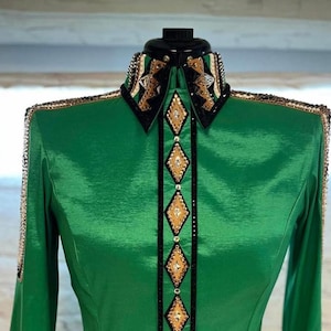 May include: A green long-sleeved shirt with a black and gold trim and rhinestones. The shirt has a pointed collar and a button-up front.