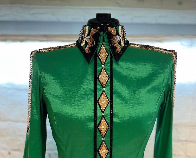 May include: A green long-sleeved shirt with a black and gold trim and rhinestones. The shirt has a pointed collar and a button-up front.