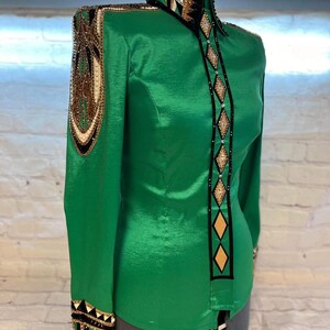 May include: A green, long-sleeved shirt with black and gold trim. The shirt has a high collar and a button-up front. The trim features a geometric pattern with rhinestones.