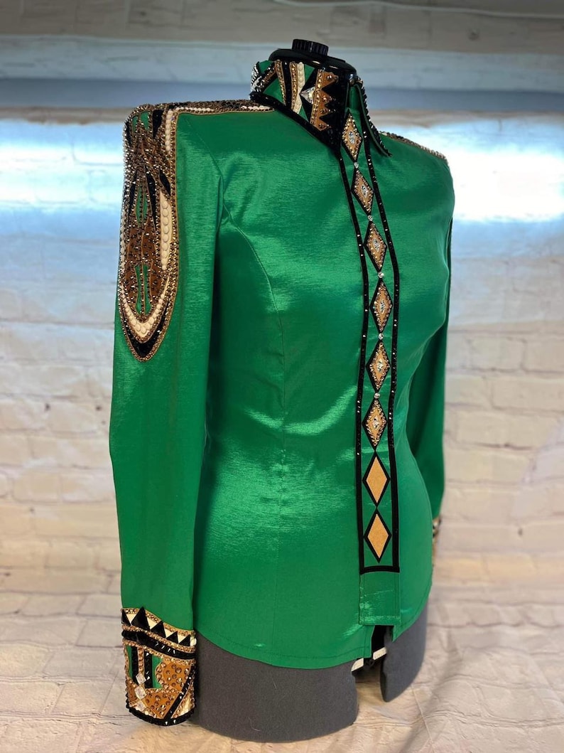 May include: A green, long-sleeved shirt with black and gold trim. The shirt has a high collar and a button-up front. The trim features a geometric pattern with rhinestones.