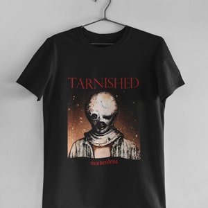 May include: Black t-shirt with a red graphic print of a person wearing a mask. The graphic has the text "Tarnished" and "maidenless" on it.