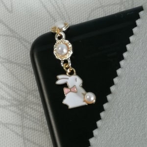 May include: A gold charm with a white bunny wearing a pink bow and holding a pearl. The charm is attached to a gold chain with pearl accents.