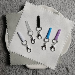 以下が含まれることがあります： シルバーのロブスタークラスプが付いた、5色の異なるシリコン製携帯電話チャーム。チャームは白、黒、水色、紫、透明です。