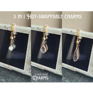 May include: Three gold-toned metal charms with clear beads and faceted pendants attached to a white device frame. The text 3 IN 1 HOT-SWAPPABLE CHARMS and Little Void CHARMS is visible. Each charm features a different shaped clear crystal-like drop.