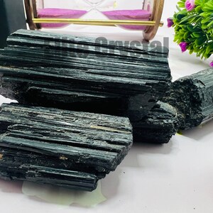 May include: Several raw, black tourmaline crystals are displayed. The crystals have a striated texture and a deep, glossy black color. The image showcases the natural, unpolished form of the mineral, highlighting its rough, textured surface.