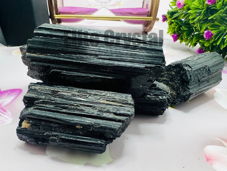 May include: Several raw, black tourmaline crystals are displayed. The crystals have a striated texture and a deep, glossy black color. The image showcases the natural, unpolished form of the mineral, highlighting its rough, textured surface.