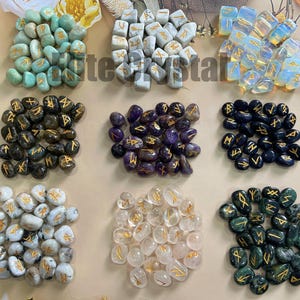 Peut inclure: Divers assortiments de pierres de runes de différentes couleurs, dont turquoise, gris et violet. Chaque pierre est ornée de symboles runiques dorés. Les pierres sont disposées en groupes, présentant différents types et couleurs de pierres.