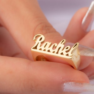 May include: Gold ring with the name "Rachel" spelled out in cursive lettering.