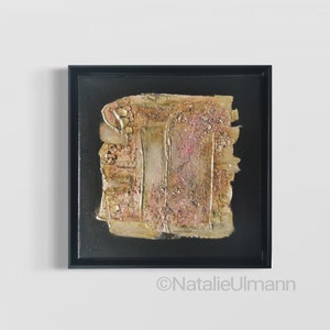 May include: Abstract painting with gold and pink textured paint on a black canvas, framed in a black frame.