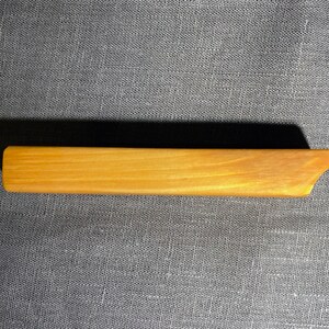Puede incluir: Una pinza para el cabello rectangular de madera con un acabado liso de color marr&oacute;n claro y un extremo inclinado y c&oacute;nico. El accesorio presenta un patr&oacute;n de veta de madera natural en toda su superficie, con un dise&ntilde;o simple, alargado y plano.