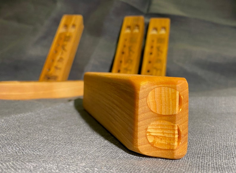 Puede incluir: Un conjunto de bloques de madera de color marr&oacute;n claro con forma rectangular y bordes redondeados. Cada bloque presenta dos hendiduras circulares en un extremo y una serie de peque&ntilde;as marcas circulares oscuras en el lateral con veta natural.