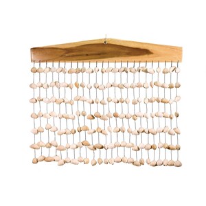 Pode incluir: Uma decoração de parede com uma parte superior de madeira com acabamento natural. Numerosas pedras pequenas, de cor clara e formato oval, são amarradas verticalmente na peça de madeira, criando uma estética texturizada e natural. As pedras são suspensas por fios finos e escuros.