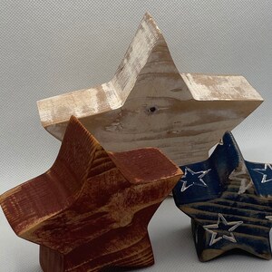 May include: Three wooden stars in red, white, and blue. The stars are painted and distressed. The white star is the largest, followed by the red star, and then the blue star.