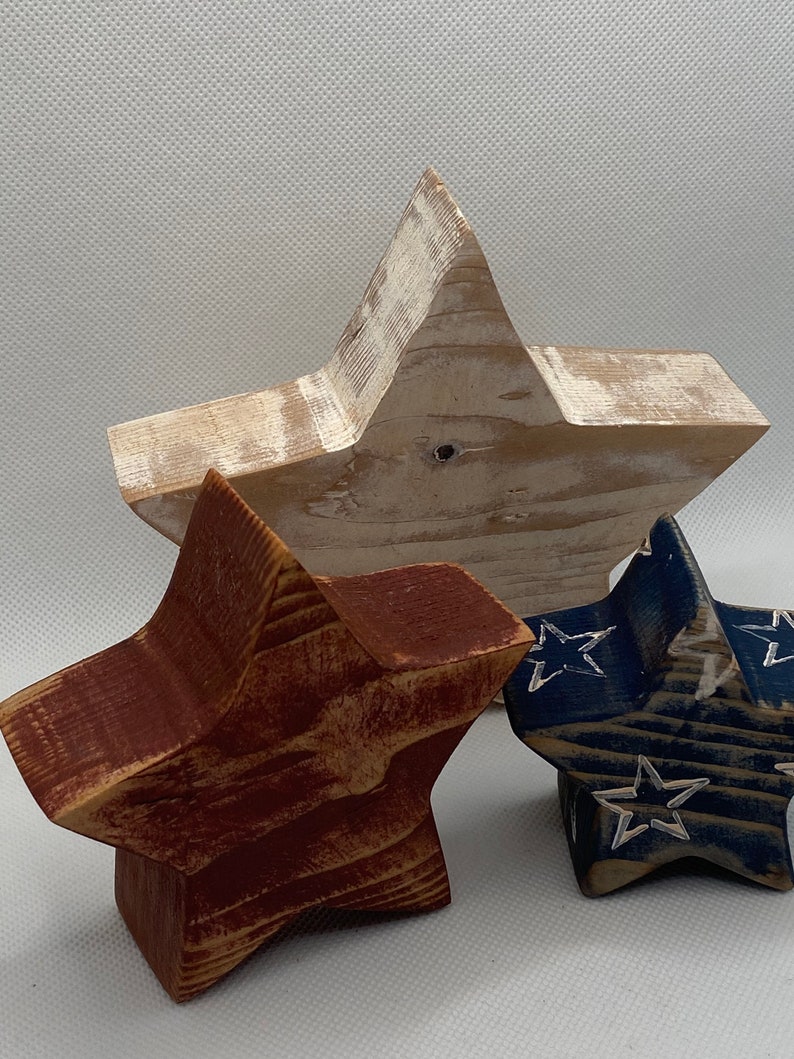 May include: Three wooden stars in red, white, and blue. The stars are painted and distressed. The white star is the largest, followed by the red star, and then the blue star.
