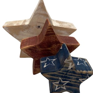 May include: Three wooden stars in red, white, and blue. The largest star is white, the middle star is red, and the smallest star is blue with white stars painted on it.